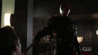 A Man In A Superhero Costume Is Holding A Sword In His Hand In A Dark Room . GIF