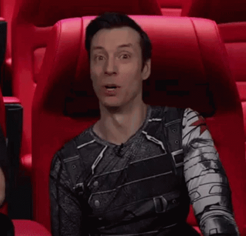 A Man In A Superhero Costume Is Sitting In A Red Chair Making A Face . GIF