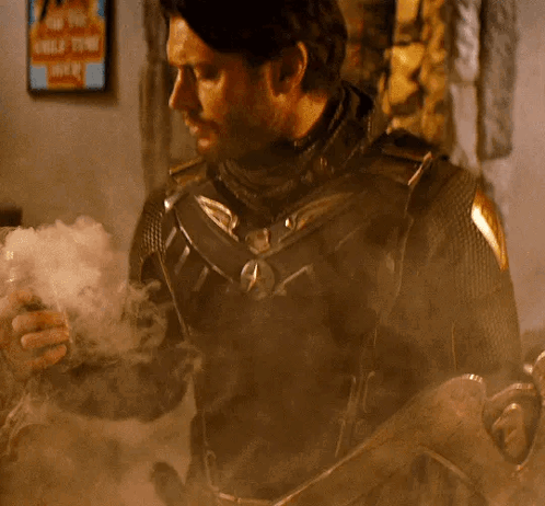 A Man In A Superhero Costume Is Smoking A Cigarette While Holding A Gun . GIF