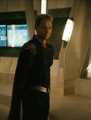 A Man In A Superhero Costume Is Standing In A Room With A Cape . GIF