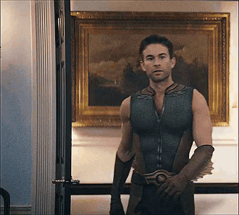 A Man In A Superhero Costume Is Standing In Front Of A Painting In A Room . GIF