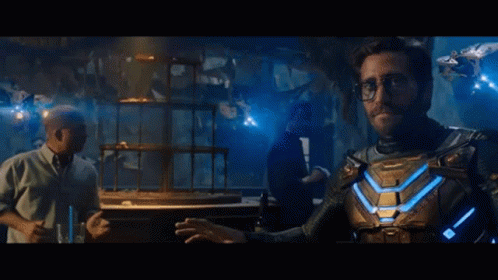 A Man In A Superhero Costume Is Standing Next To A Man In A Tuxedo In A Dark Room . GIF