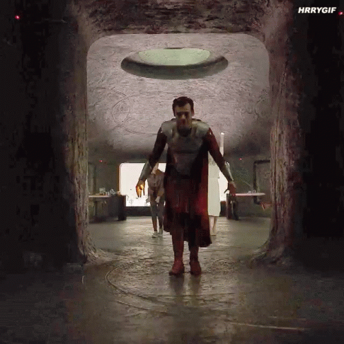 A Man In A Superhero Costume Is Walking Through A Tunnel In A Cave . GIF