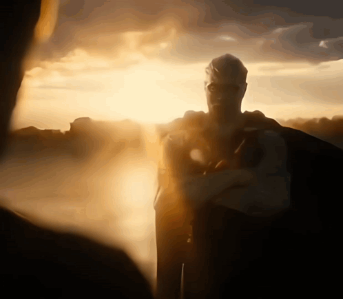 A Man In A Superhero Costume Stands In Front Of The Sun GIF