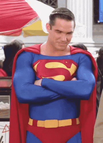 A Man In A Superman Costume Has His Arms Crossed And A Red Cape GIF