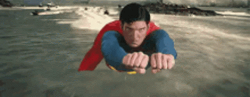 A Man In A Superman Costume Is Flying Over The Water . GIF