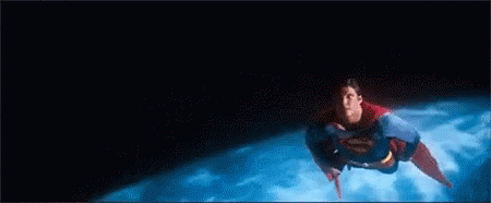 A Man In A Superman Costume Is Flying Through The Air Over A Planet . GIF