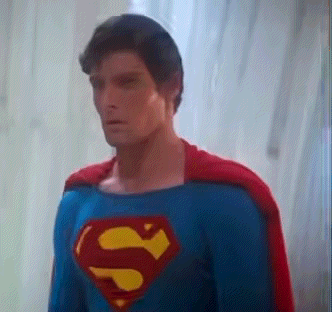 A Man In A Superman Costume Is Standing In Front Of A Window GIF