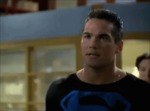 A Man In A Superman Costume Is Standing In Front Of A Window . GIF