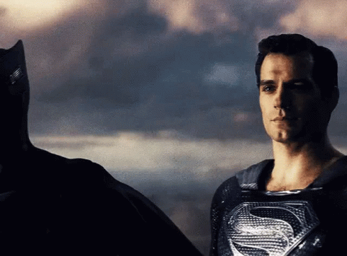 A Man In A Superman Costume Is Standing Next To A Man In A Batman Costume GIF