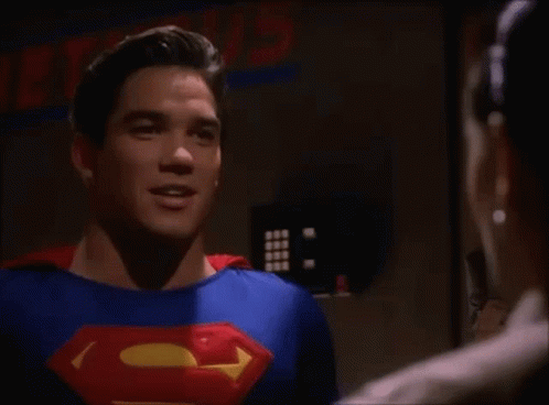 A Man In A Superman Costume Is Talking To Another Man In A Room . GIF