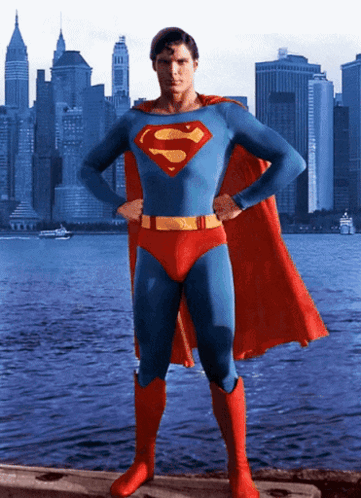 A Man In A Superman Costume Stands In Front Of A City Skyline With His Hands On His Hips GIF