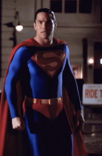 A Man In A Superman Costume Stands In Front Of A Sign That Says Ride T. GIF