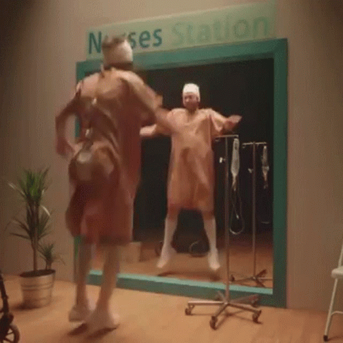 A Man In A Surgical Gown Is Dancing In Front Of A Sign That Says Nurse Station GIF