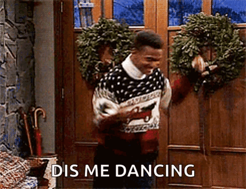 A Man In A Sweater Is Dancing In Front Of A Door With A Wreath Hanging On It . GIF