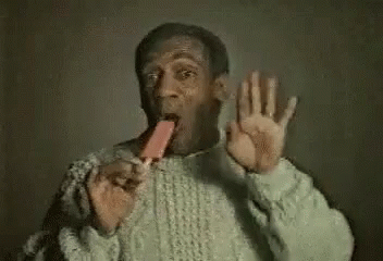 a man in a sweater is eating an ice cream cone and making a funny face .