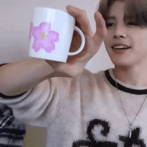 A Man In A Sweater Is Holding A Mug With A Pink Flower On It GIF