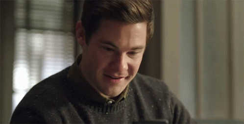 A Man In A Sweater Is Smiling And Looking At His Phone GIF