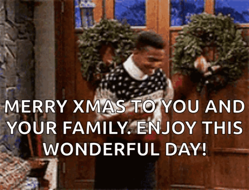 A Man In A Sweater Is Standing In Front Of A Door With A Wreath On It And Says Merry Xmas GIF