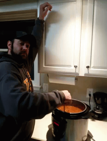 A Man In A Sweatshirt That Says ' Tigers ' On It Is Pouring Soup Into A Pot GIF