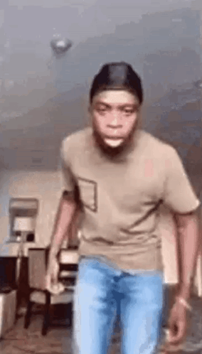 A Man In A T-Shirt And Jeans Is Standing In A Living Room . GIF