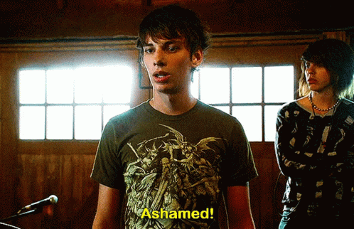 A Man In A T-Shirt That Says " Ashamed " Stands In Front Of A Microphone GIF