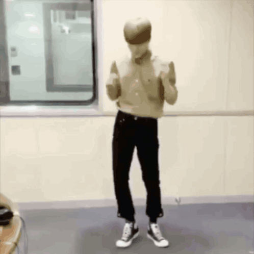 A Man In A Tan Shirt And Black Pants Is Standing In A Room . GIF