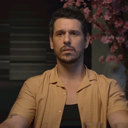A Man In A Tan Shirt Holds Up His Hand GIF