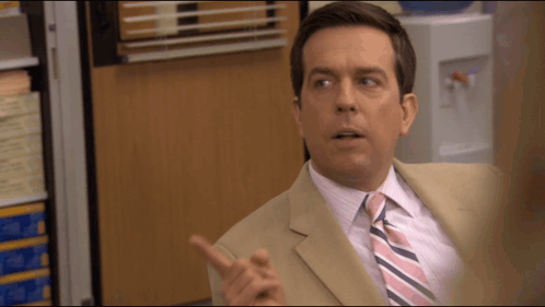 A Man In A Tan Suit And Pink And Blue Striped Tie Is Pointing GIF