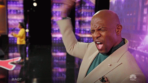 Man In Tan Suit Raising Fist In Front Of NBC Sign GIF