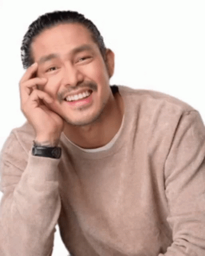 A Man In A Tan Sweater Is Smiling With His Hand On His Chin GIF
