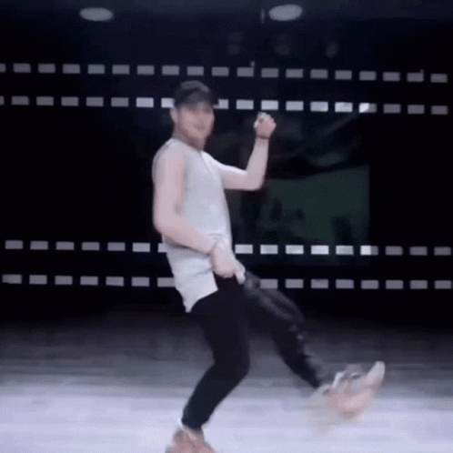 A Man In A Tank Top And Black Pants Is Dancing On A Stage . GIF