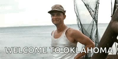 A Man In A Tank Top And Hat Is Standing On A Boat In The Ocean And Says `` Welcome To Oklahoma '' . GIF