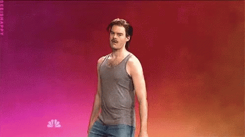 A Man In A Tank Top And Jeans Is Standing On A Stage . GIF