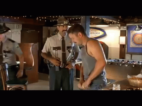 A Man In A Tank Top Is Standing In Front Of A Police Officer In A Bar GIF