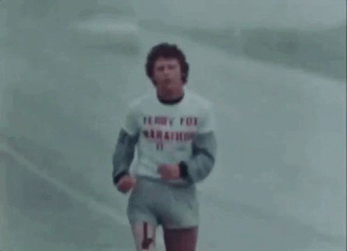 A Man In A Terry Fox Marathon Shirt Is Running On A Road . GIF
