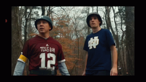 A Man In A Texas A & M Jersey Stands Next To Another Man GIF