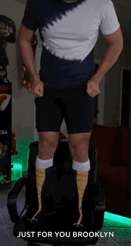 A Man In A Tie Dye Shirt And Black Shorts Is Standing On A Chair With The Words Just For You Brooklyn Above Him GIF