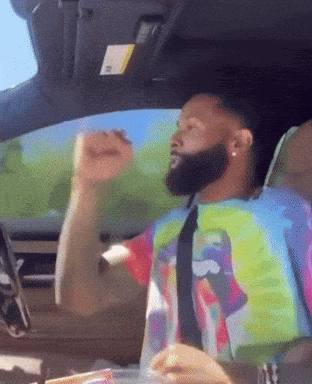 A Man In A Tie Dye Shirt And Tie Is Driving A Car GIF