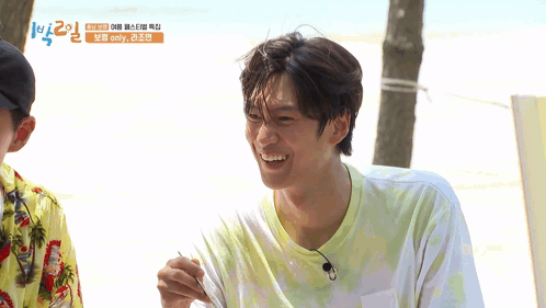 A Man In A Tie Dye Shirt Is Smiling In Front Of A Sign That Says ' Emily ' On It GIF