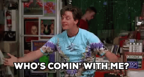 A Man In A Tie Dye Shirt Is Standing In Front Of A Record Store . GIF