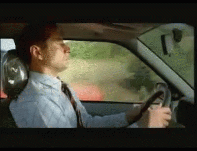 A Man In A Tie Is Driving A Car GIF
