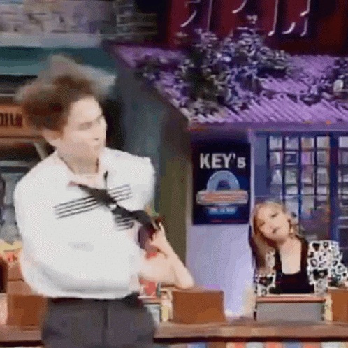 A Man In A Tie Is Standing In Front Of A Sign That Says Key 'S On It . GIF