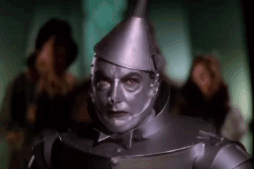 A Man In A Tin Man Costume From The Wizard Of Oz Is Standing In Front Of A Crowd Of People . GIF