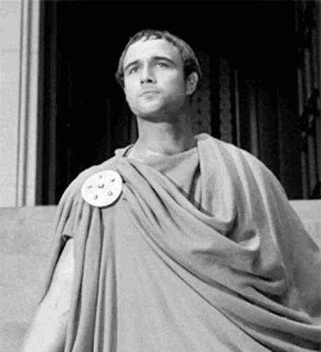 A Man In A Toga Is Standing In Front Of A Building . GIF
