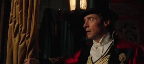 A Man In A Top Hat And Bow Tie Is Standing In A Dark Room . GIF