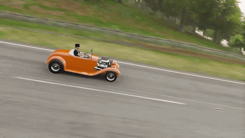 a man in a top hat drives an orange car on a road