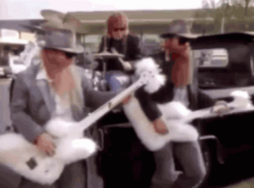A Man In A Top Hat Is Playing A Guitar In Front Of A Car . GIF