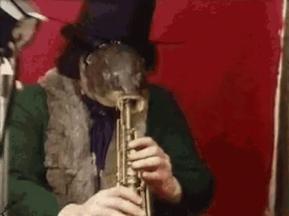 A Man In A Top Hat Is Playing A Trumpet In Front Of A Red Background . GIF