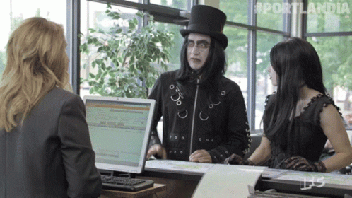 A Man In A Top Hat Is Talking To Two Women In Front Of A Computer Screen That Says Portlandia On It GIF